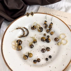 Macro view of vintage tiger eye earrings set with gold heart charms on ceramic tray