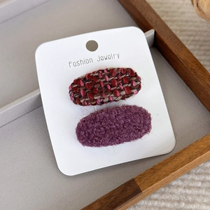 Gros plan de barrettes en tweed rose et polaire violette sur une carte blanche