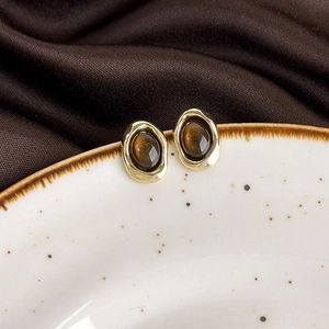 Close-up of vintage golden tiger eye earrings on a white textured ceramic dish