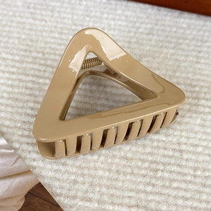 Détail d'une pince à cheveux triangulaire ajourée kaki sur un fond en peluche blanc