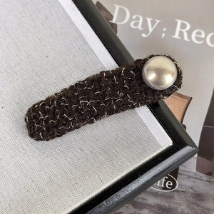 Close-up of brown knit hair clip with silver thread and metallic button detail