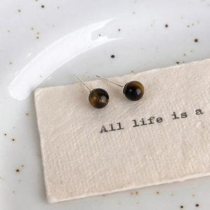 Macro shot of vintage tiger eye stud earrings on textured beige paper with silver needles