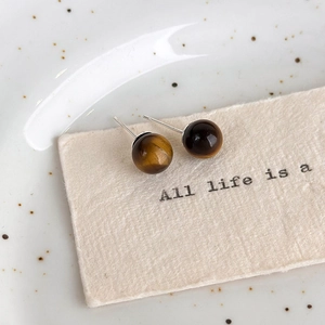 Macro shot of tiger eye stud earrings on textured card over white ceramic plate