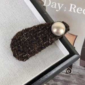 Macro shot of brown tweed hair clip with gold threads and a central pearl detail
