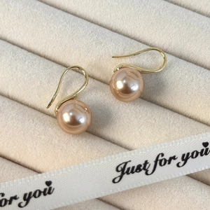 Primer plano de pendientes de perlas champán en un joyero de terciopelo beige de alta gama