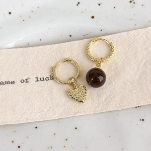 Detail of asymmetric gold earrings with heart charm and dark brown translucent bead