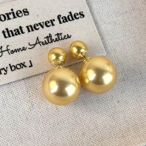 Detailed macro view of French double-sided gold pearl earrings on a stylish canvas backdrop