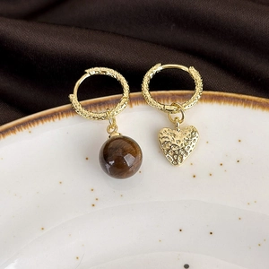 Detail of asymmetric gold hoop earrings with tiger eye bead and hammered heart pendant