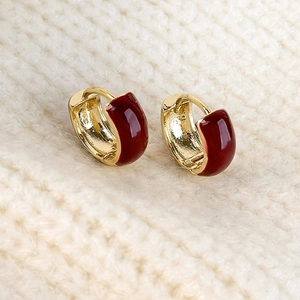 Detail view of gold-plated red enamel hoop earrings on a warm knitted sweater background