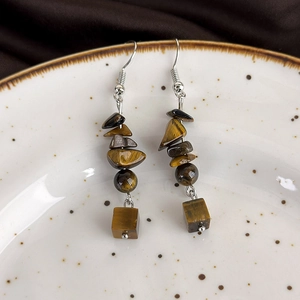 Macro detail of bohemian tiger eye stone earrings on a textured white plate background