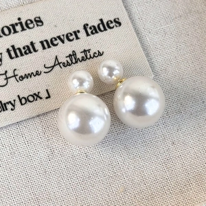 Close-up of double-sided pearl earrings with gold base on grey linen background