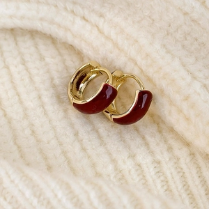 Close-up of golden hoop earrings with red enamel detail on white knit sweater texture