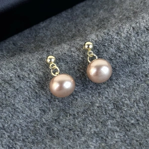 Close-up of champagne pearl drop earrings with golden spherical studs on grey fabric