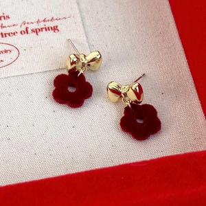 Detail of gold bow earrings with red velvet flower charms on a textured gift display card