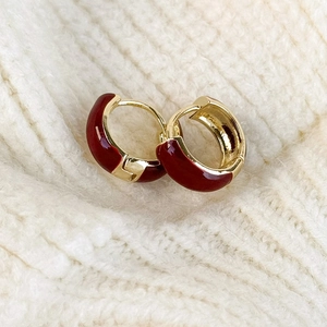 Detailed view of red enamel hoop earrings on white knit fabric with gold plating finish