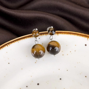 Detailed close-up of vintage tiger eye stone drop earrings on a ceramic dish