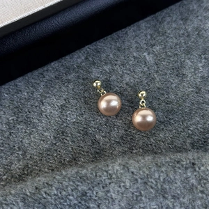 Macro shot of elegant champagne gold pearl stud earrings on a grey knit texture surface