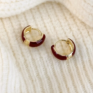 Detail of red enamel gold hoop earrings displayed on a cozy knit fabric background