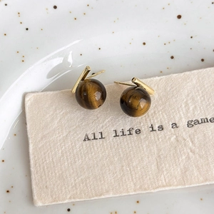 Detailed macro view of vintage tiger eye stone stud earrings on textured beige paper
