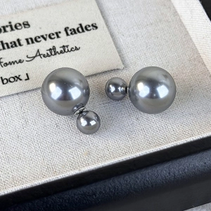 Detailed view of dual-sided dark grey pearls earrings on elegant white textured fabric
