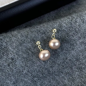Detailed close-up of champagne pearl drop earrings with golden studs on grey knit