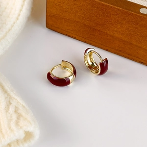 Elegant gold huggie hoop earrings with red drip glaze finish on a soft knitted background
