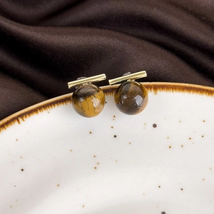 Detailed close-up of tiger eye stone earrings with gold metal bars on ceramic plate