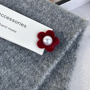 Macro detail of red velvet flower clip featuring a central pearl and soft flocked texture