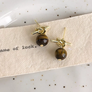 Close-up of golden knotted earrings with brown tiger eye stone beads on a ceramic plate