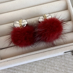 Dettaglio di orecchini a pompon bordeaux con cuore d'argento e catena dorata