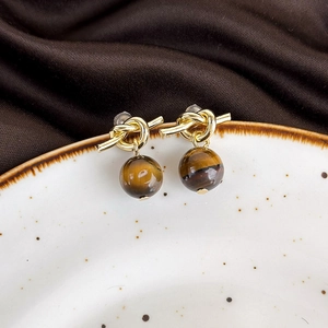 Detailed macro view of knotted golden earrings with tiger eye stone on ceramic plate