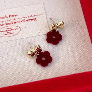 Macro detail of golden bow earrings with red flocked flower charms on a beige velvet box