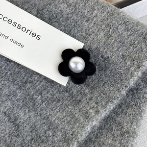 Close-up of a velvet flower hair clip with a faux pearl center on a knit background
