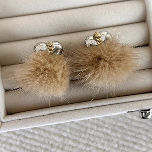 Dettaglio orecchini a cuore con pompon e catena dorata su espositore in velluto beige