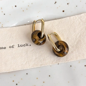 Detail of vintage tiger eye stone earrings with gold hoops on a rustic ceramic background