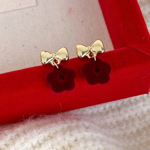 Macro shot of gold bow stud earrings with deep red flocked flower pendants on red velvet