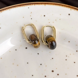 Close-up of gold U-shaped earrings with polished tiger eye stones on a ceramic plate