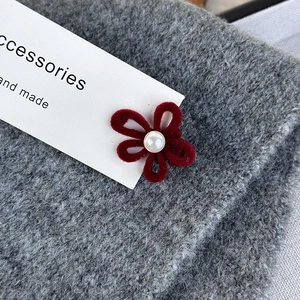 Detail of a dark red velvet flower hair clip with a pearl center on a knitted fabric