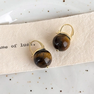 Close-up of vintage tiger eye stone earrings with golden hooks on textured paper