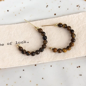 Macro shot of C-shaped tiger eye beaded earrings with golden metal studs on display card