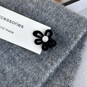 Macro detail of a black velvet floral hair clip with a pearl center on knit fabric
