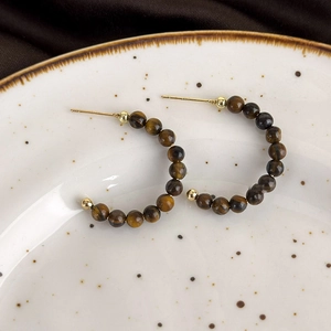 Detail view of tiger eye stone C-shaped hoop earrings with S925 silver studs on ceramic