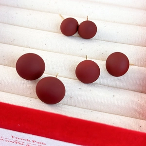 Cinq boucles d'oreilles rondes rouge foncé mat avec tiges dorées sur plateau blanc