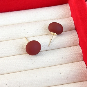 Vue macro de boucles d'oreilles rouges mates sur velours crème avec tiges dorées