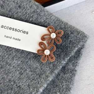 Detail view of two brown velvet flower hair clips with white pearls and hollowed petal design