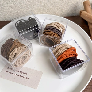 Close-up of caramel elastic hair ties in clear acrylic boxes with woven texture
