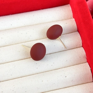 Gros plan de boucles d'oreilles ovales rouge foncé mat avec tiges dorées sur plateau beige