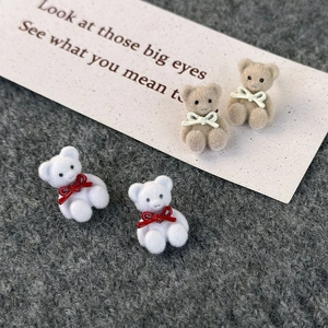 Close-up of cute flocked bear earrings with bows on gray knitted fabric backdrop