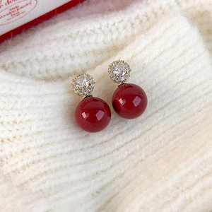 Dettaglio di orecchini vintage con perle rosse e zirconi su sfondo in maglia bianca