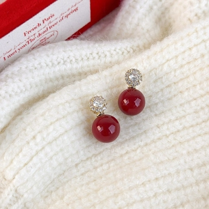 Dettaglio di eleganti orecchini di perle rosse con zirconi su sfondo in maglia beige